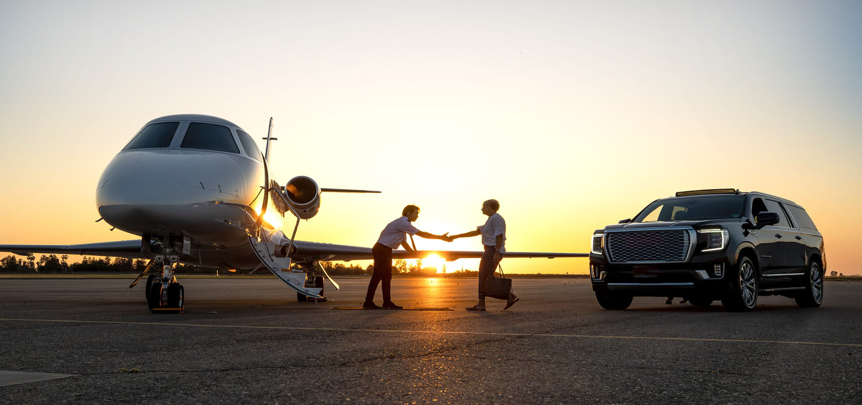 Two men on a tarmac shake hands as a jet and a black SUV stand by at sunset, symbolizing a business transfer or travel moment.