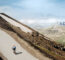 Cyclist riding a road bike on a winding mountain pass with rocky slopes and patches of snow under a blue sky.