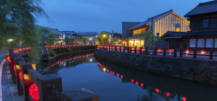 Evening canal lined with red lanterns and traditional buildings glowing beside calm water.