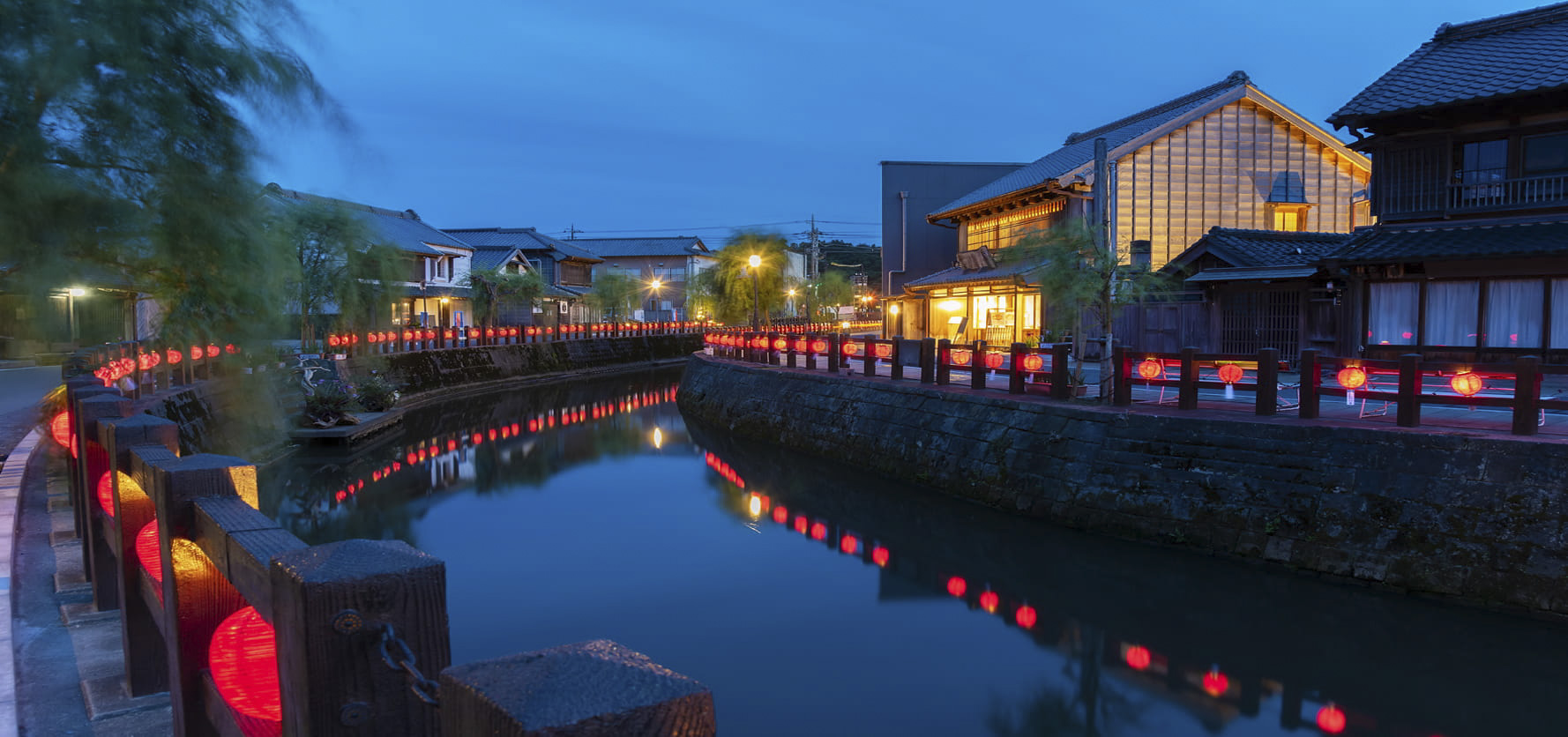 Evening canal lined with red lanterns and traditional buildings glowing beside calm water.